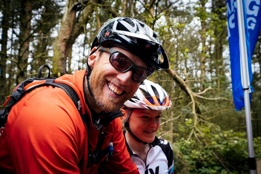 Male cyclist in sunglasses and cycling helmet smiling at the camera with his child.