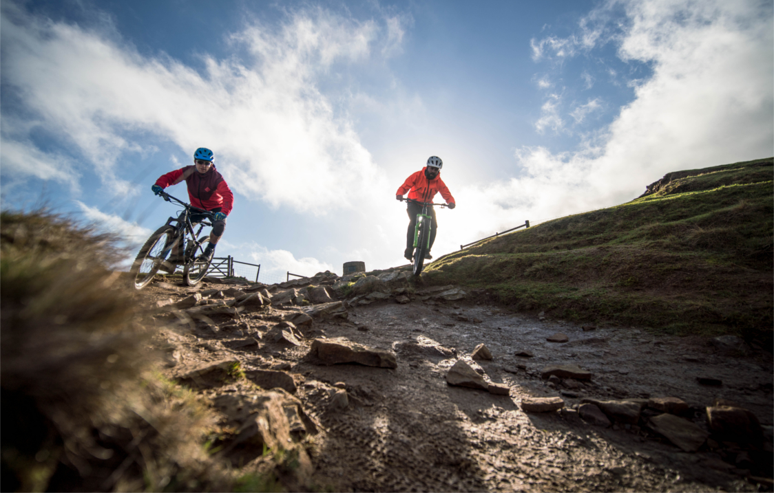 Two people mountain biking down a slope out in the countryside.