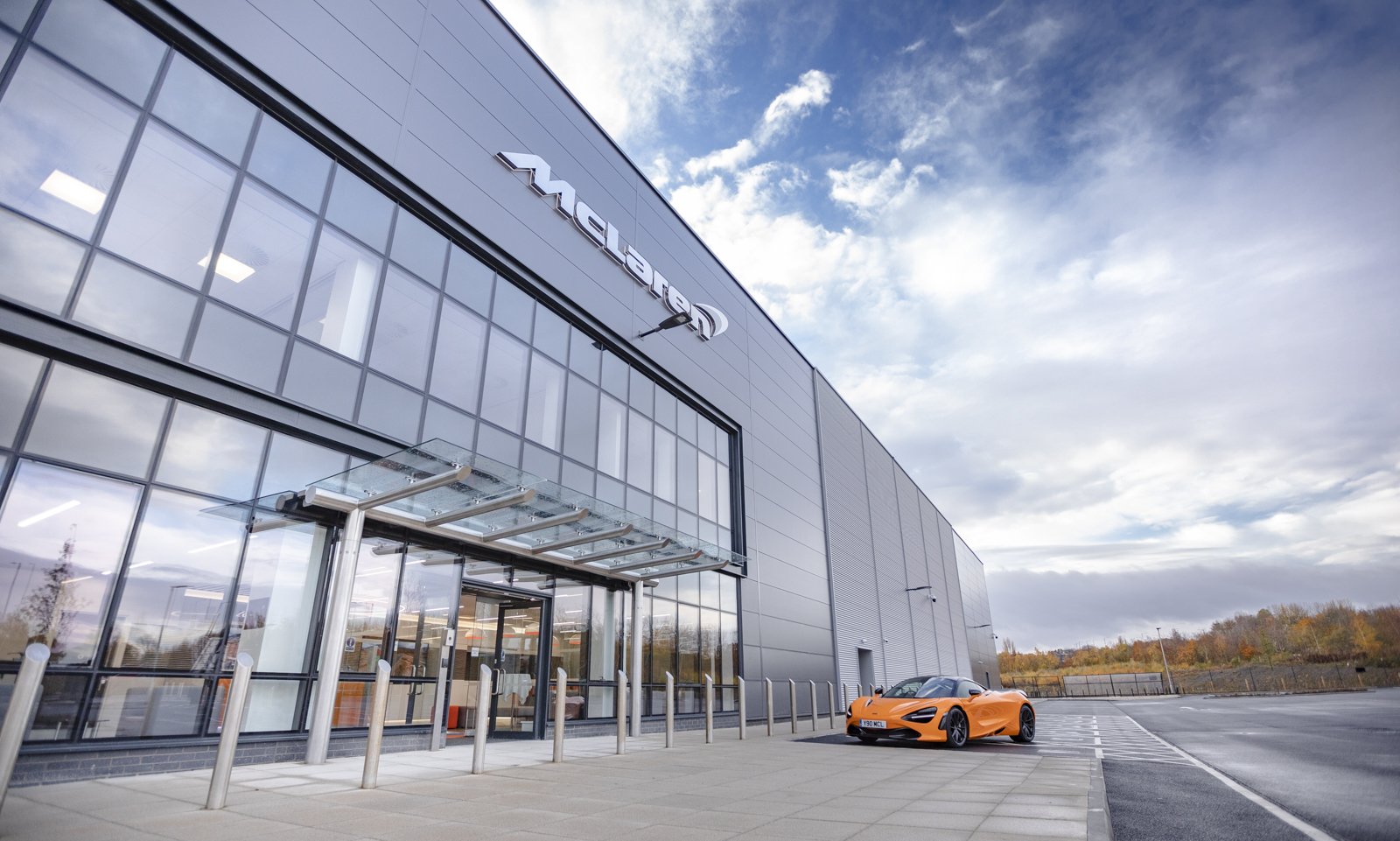 An orange McLaren car parked outside the glass McLaren building at The Advanced Manufacturing Innovation District.