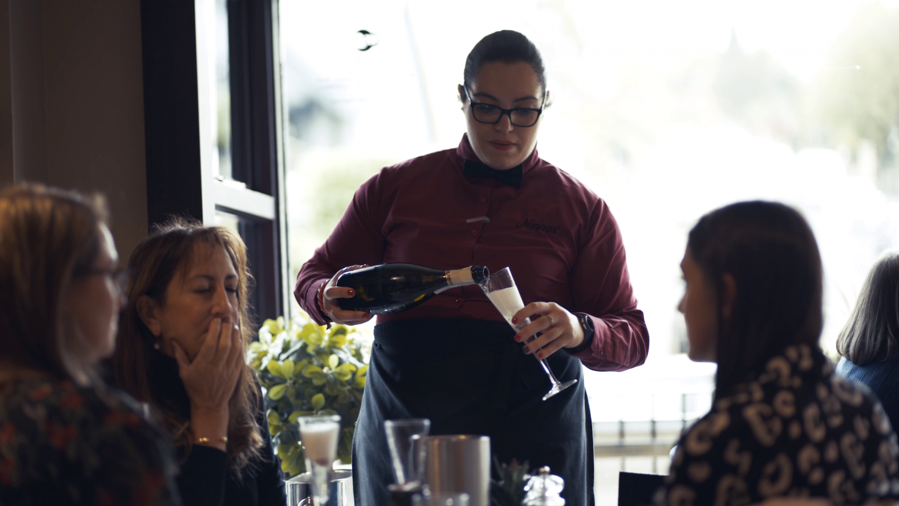 A member of staff pours sparkling wine for a table of guests at Nonnas Restaurant.