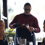 A member of staff pours sparkling wine for a table of guests at Nonnas Restaurant.