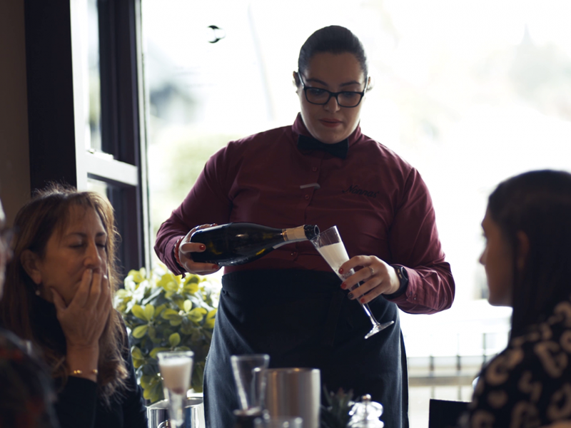 A member of staff pours sparkling wine for a table of guests at Nonnas Restaurant.