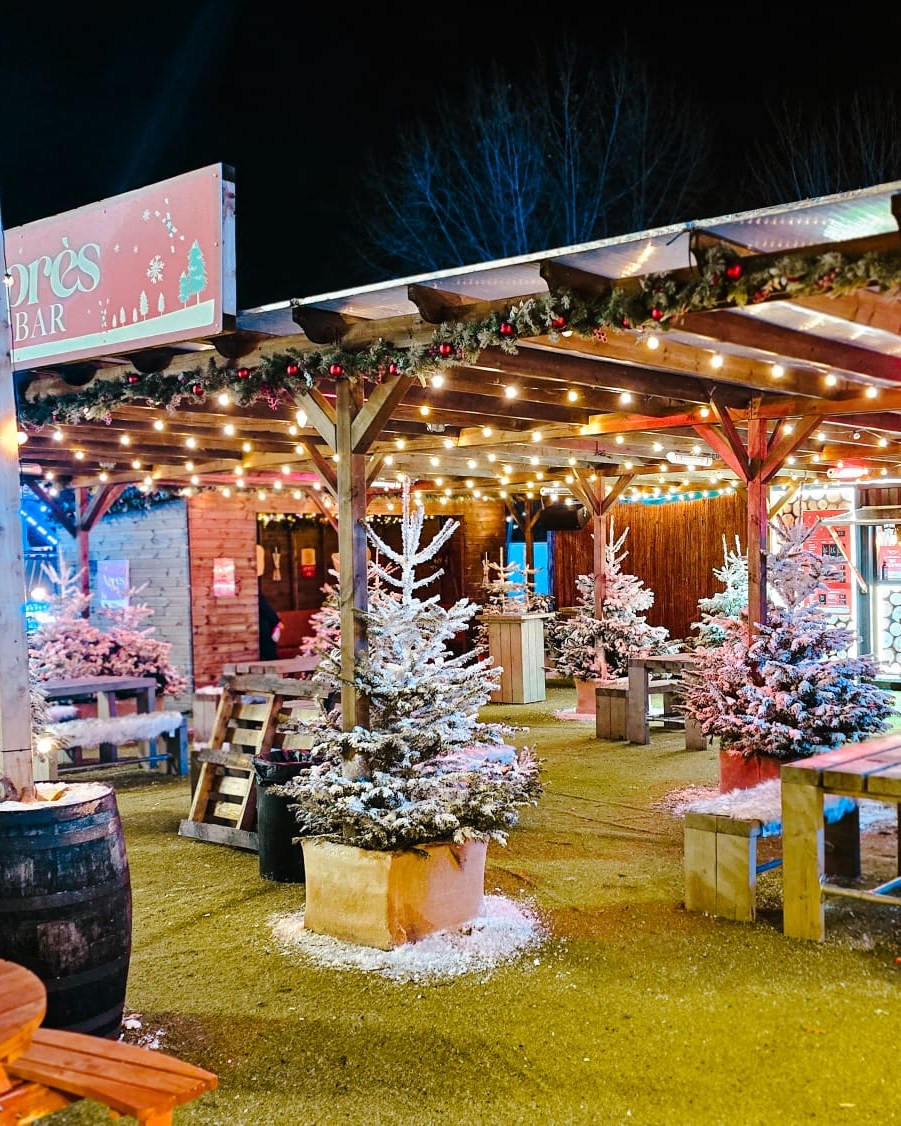 The Après Bar decorated with snowy Christmas trees in between log cabin style tables and chairs at Meadowhall's Magical Winterland 