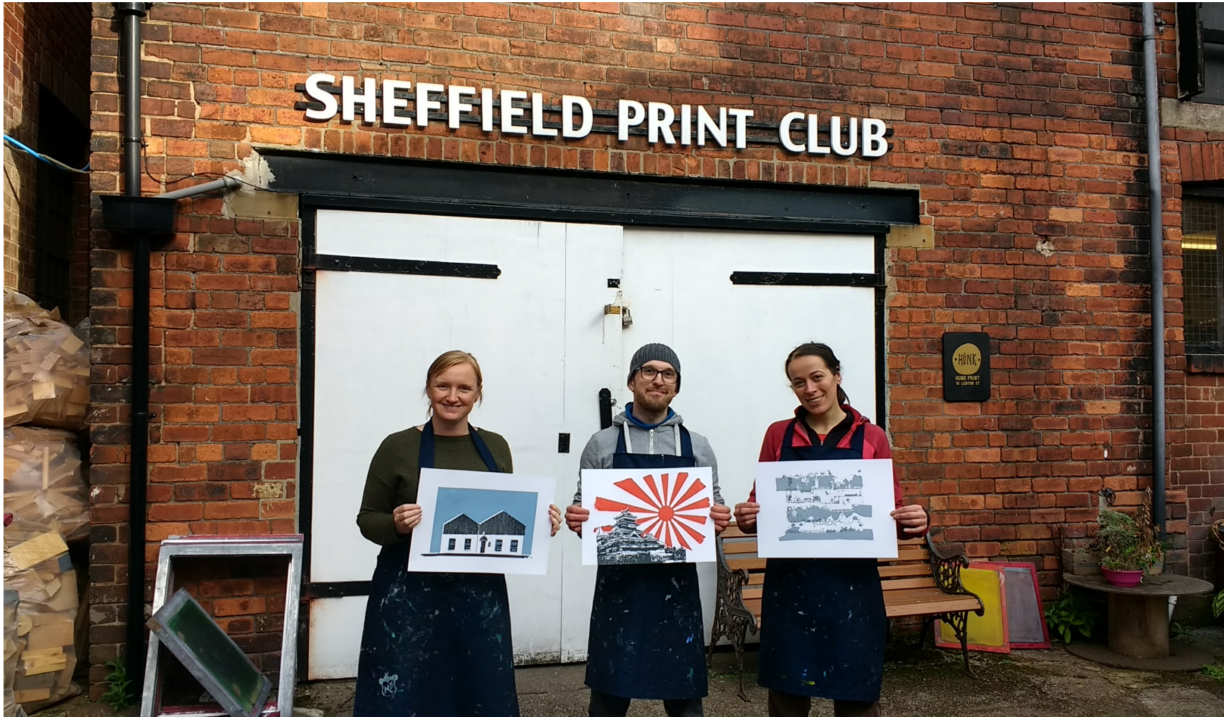 Three people standing outside Sheffield Print Club holding prints they have made.