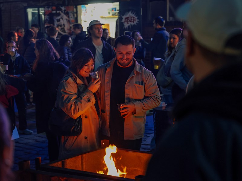 Crowds in the outside courtyard at Peddler Market, warming themselves around a fire pit while sipping drinks.