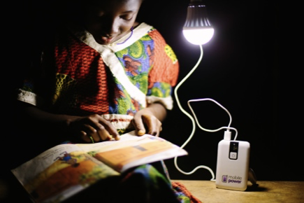 A child reads a story book, lit by a single bulb.