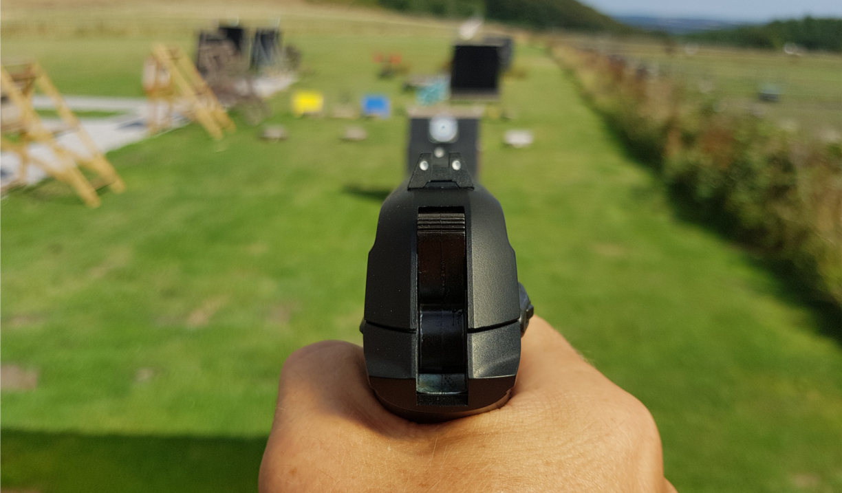 A hand holding a pistol that is aimed at a target on a shooting range.