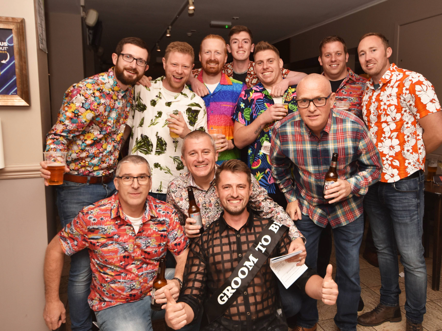 A group of men enjoying a stag do. One of the men wears a sash that says 'Groom to be'.