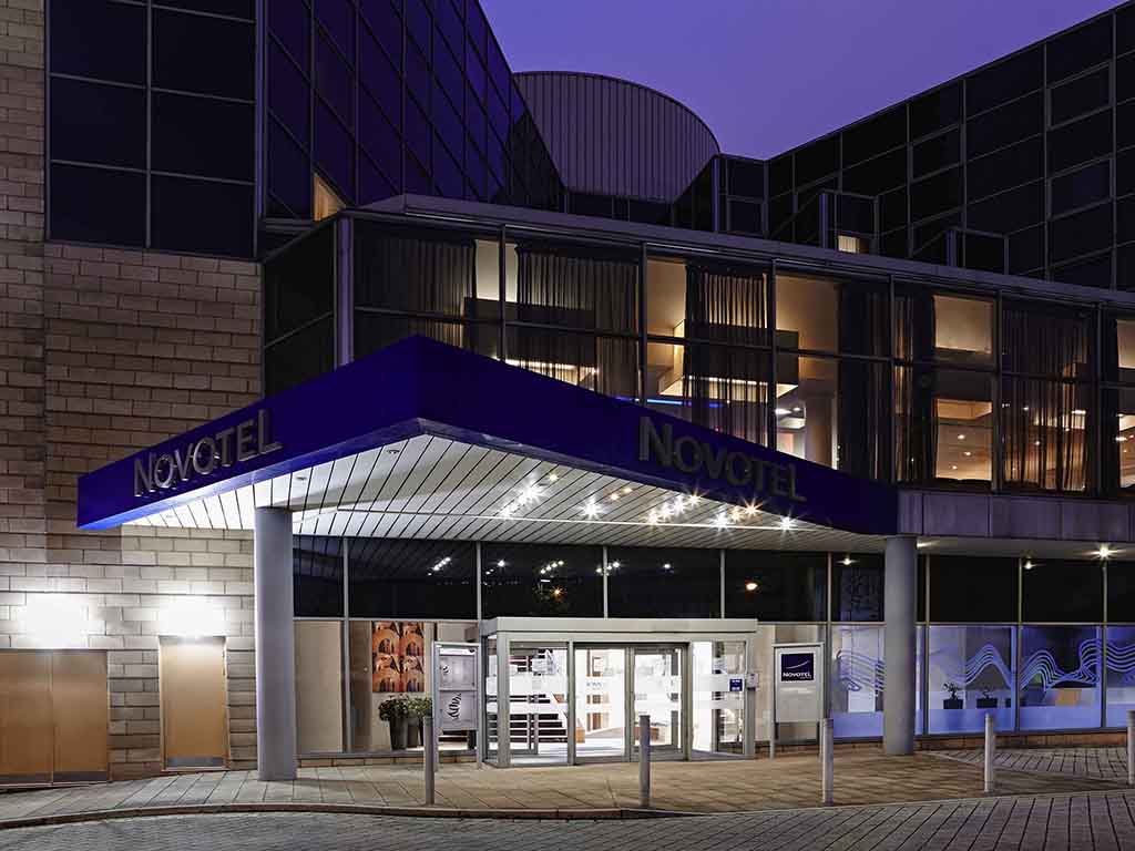 Exterior view of the Novotel hotel at night with its entrance brightly lit.