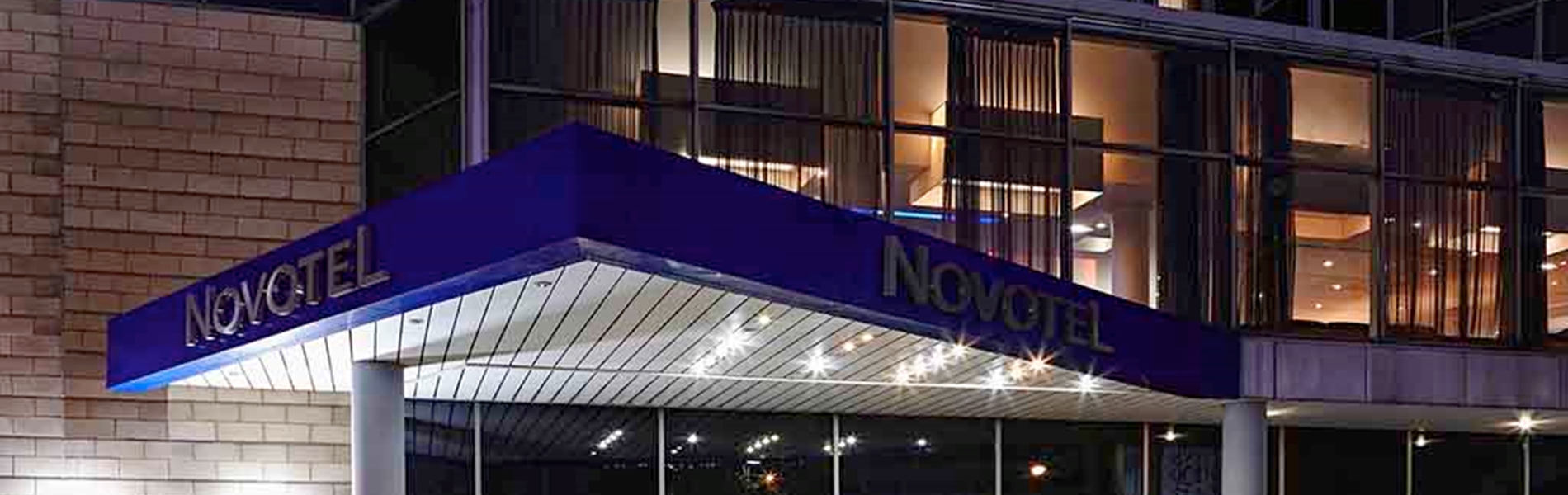 Exterior view of the Novotel hotel at night with its entrance brightly lit.
