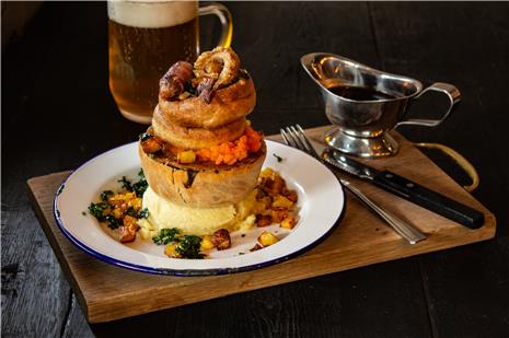 A Pieminister pie, on a table, alongside a gravy boat and a glass of beer.