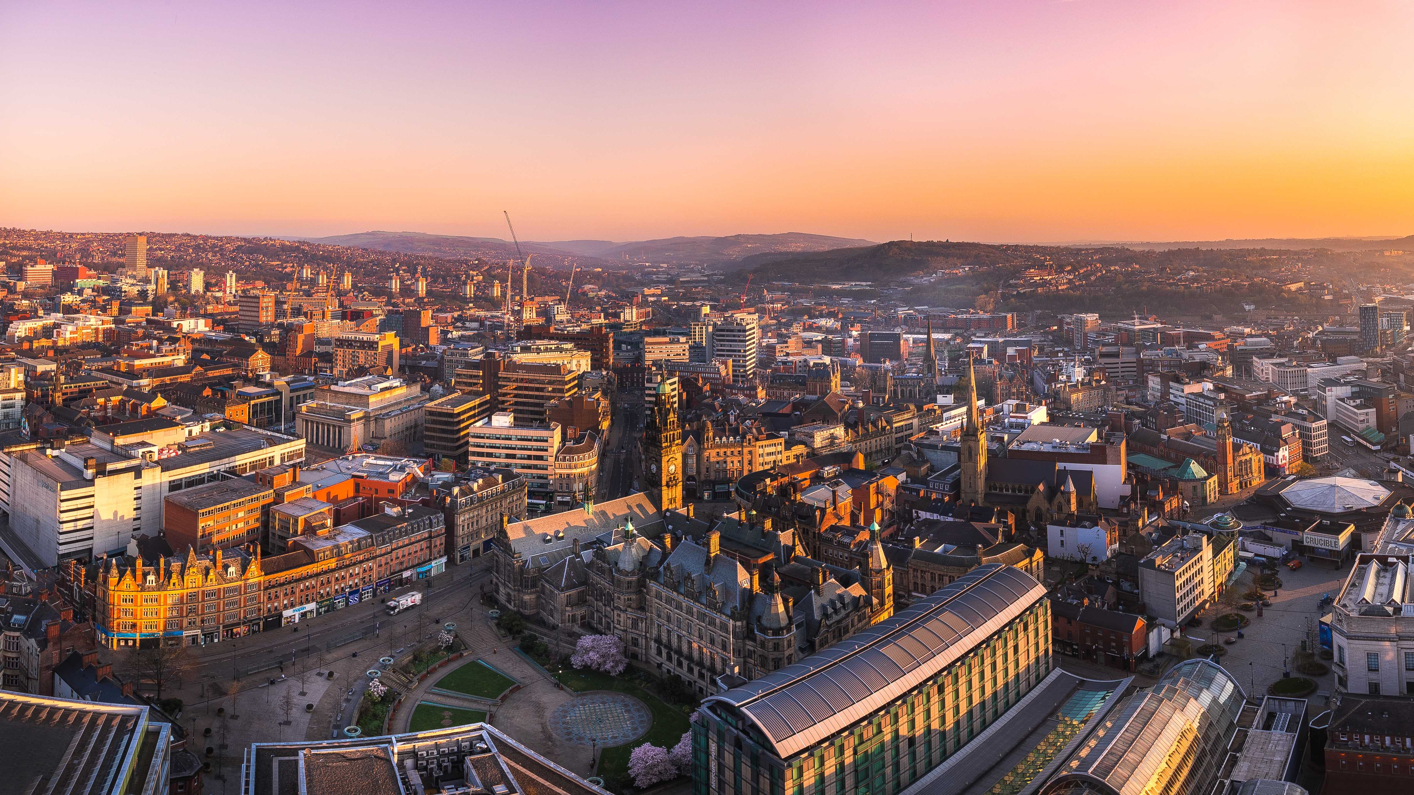 A panoramic photograph of Sheffield city centre at sunrise, that stretches out to the countryside beyond. 