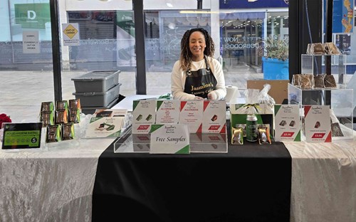 Angelina from Olga & Asquith Products Ltd standing behind a display table of Jasmine’s Jamaican Rum Cakes and Ginger Cakes at a market stall,