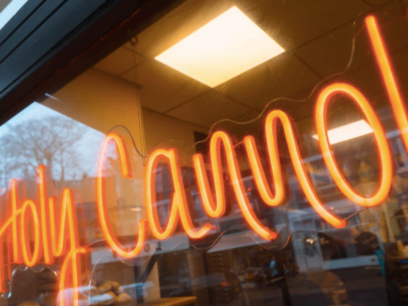 An orange neon sign that reads 'Holy Cannoli'.