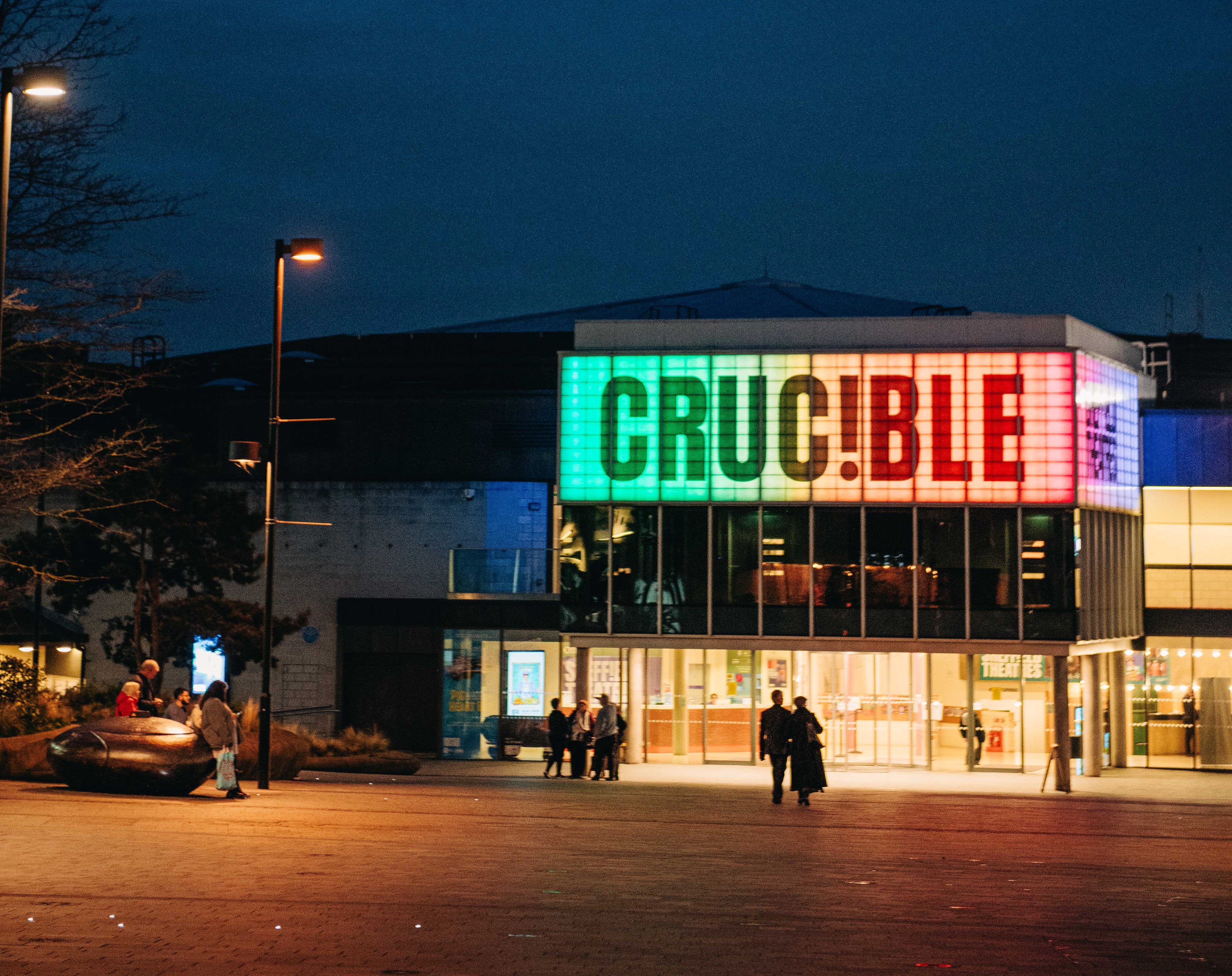 Exterior of the Crucible theatre at night with the iconic sign lit up in multi colours 
