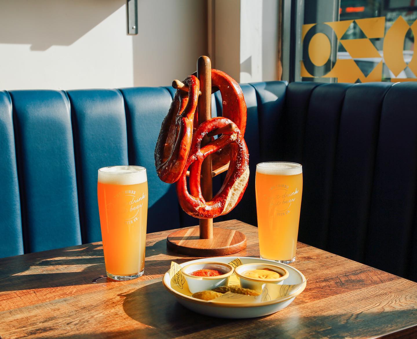 Two glasses of beer and warm pretzels on a table next to a window.