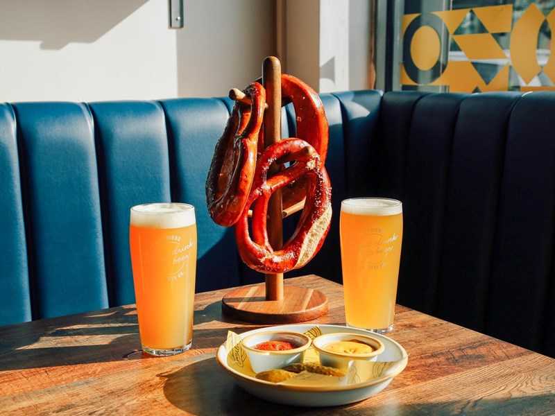 Two glasses of beer and warm pretzels on a table next to a window.