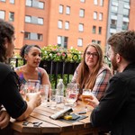 People sat round a table, outdoors, enjoying a drink at The Riverside Kelham.