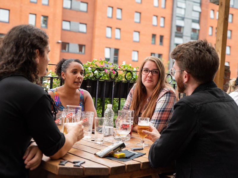 People sat round a table, outdoors, enjoying a drink at The Riverside Kelham.