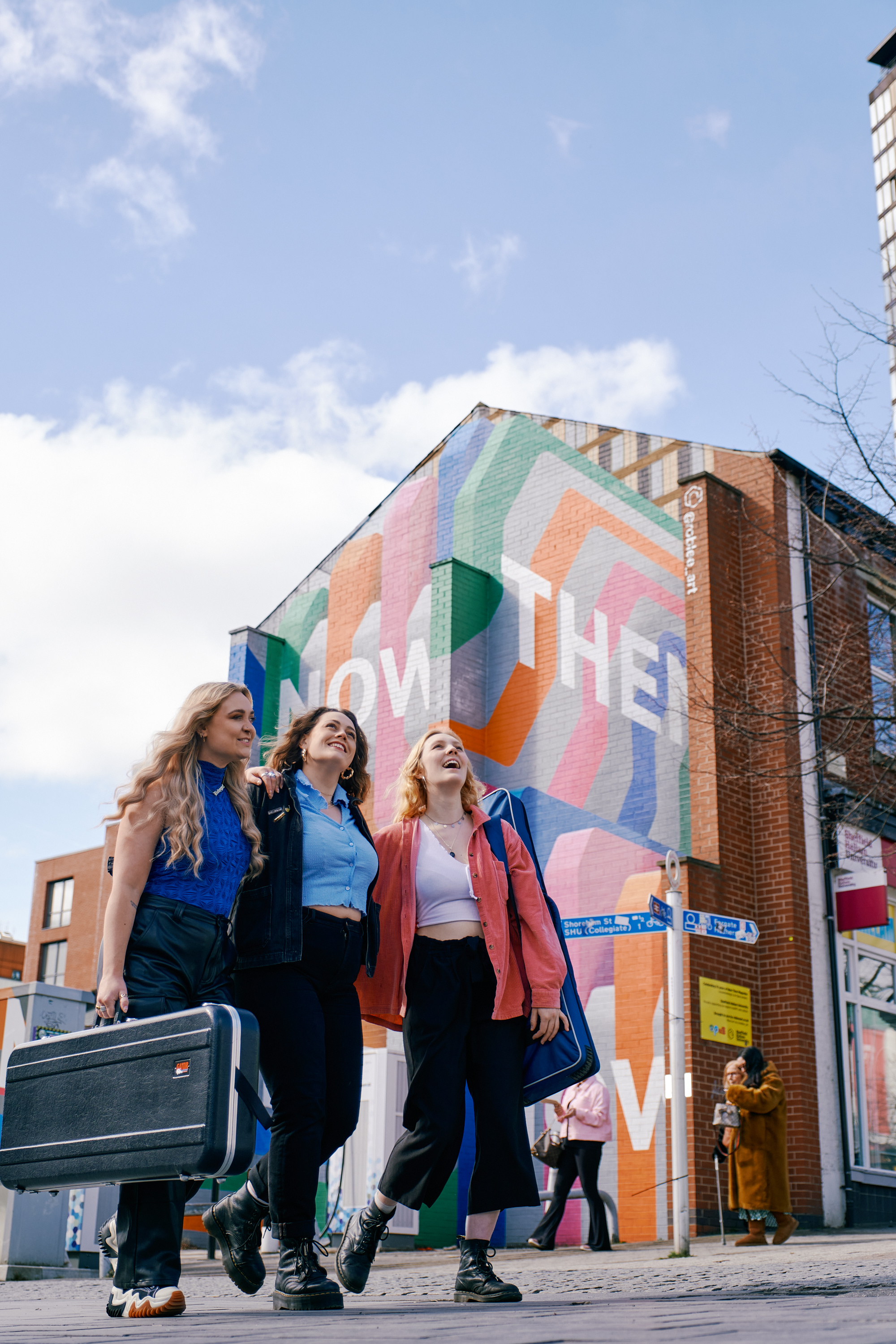 Three women stand in front of the Now Then mural on Howard Street.