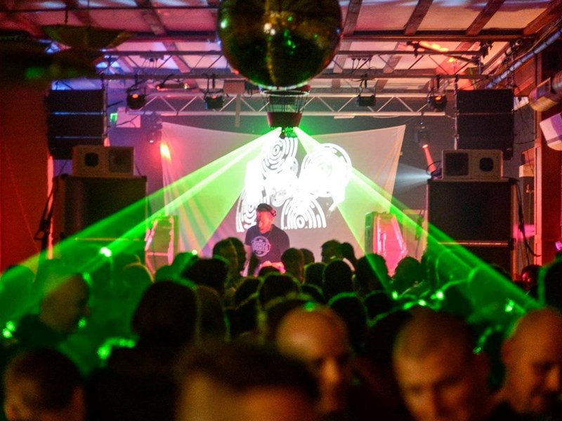A crowd dances to a DJ, with green lazers lighting the dancers.