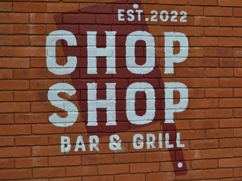 The Chop Shop Bar & Grill logo painted on a red brick wall.